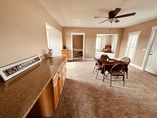 carpeted dining area with baseboards, ceiling fan, and stairs