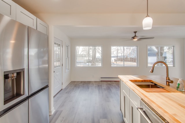 kitchen with butcher block counters, white cabinetry, baseboard heating, stainless steel fridge, and pendant lighting