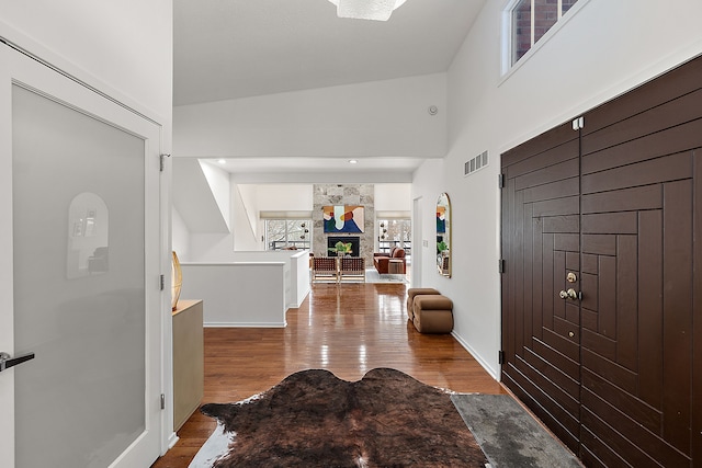 entryway featuring a fireplace, visible vents, a towering ceiling, wood finished floors, and baseboards