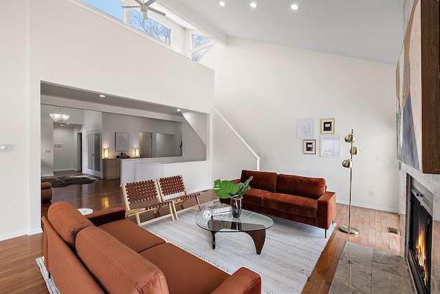 living room featuring high vaulted ceiling, wood finished floors, a fireplace with flush hearth, and baseboards