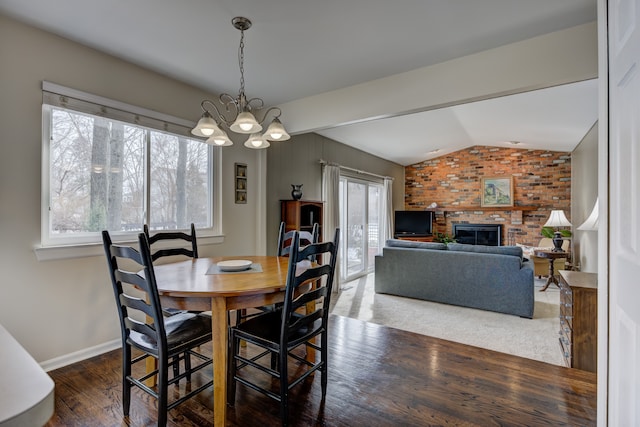 dining space featuring lofted ceiling, dark wood-type flooring, an inviting chandelier, brick wall, and a brick fireplace