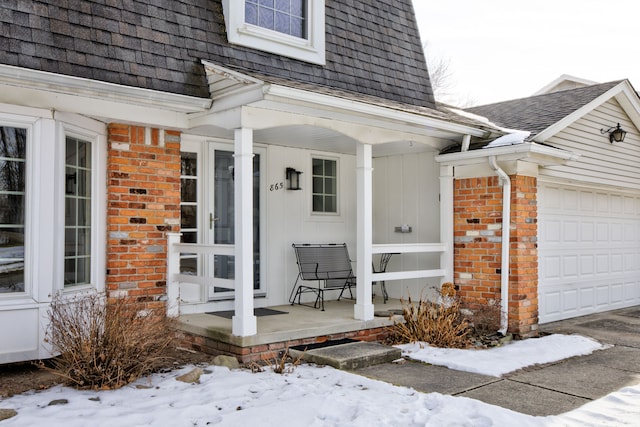 snow covered property entrance featuring a porch and a garage