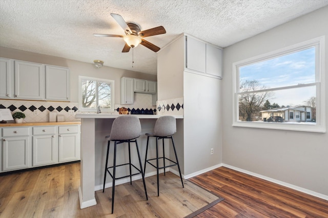 kitchen featuring tasteful backsplash, wood-type flooring, a breakfast bar area, and white cabinets