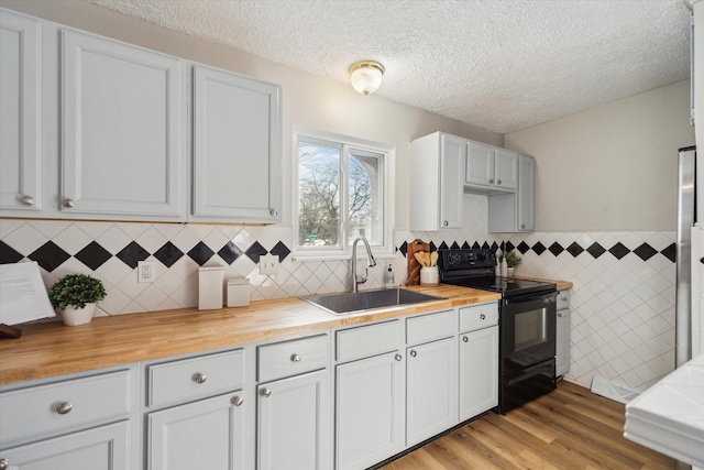 kitchen featuring butcher block countertops, white cabinetry, sink, black electric range, and light hardwood / wood-style flooring