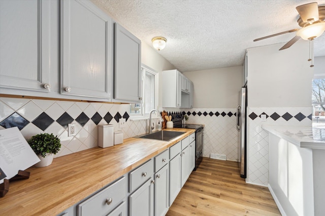 kitchen with butcher block countertops, sink, a textured ceiling, light wood-type flooring, and black / electric stove