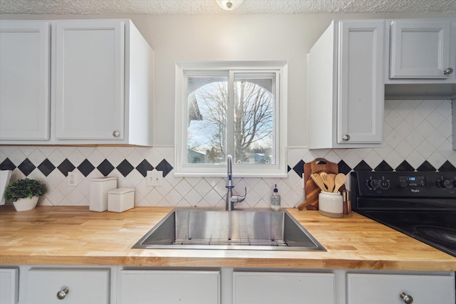 kitchen featuring sink, butcher block counters, black range with electric stovetop, white cabinetry, and a textured ceiling