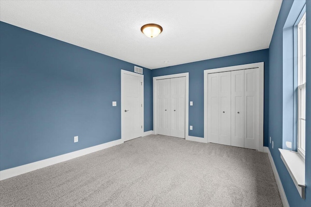 unfurnished bedroom featuring two closets, carpet floors, and a textured ceiling