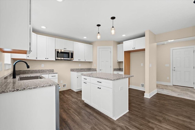 kitchen with pendant lighting, sink, white cabinets, a center island, and light stone counters