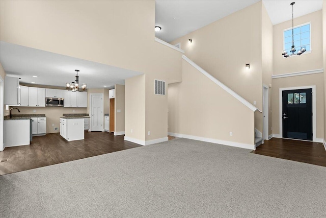 unfurnished living room featuring sink, a chandelier, dark carpet, and a high ceiling