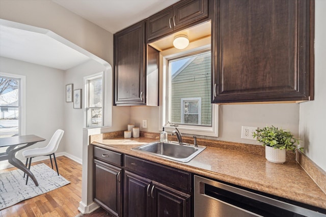 kitchen with dark brown cabinetry, sink, stainless steel dishwasher, and light hardwood / wood-style floors