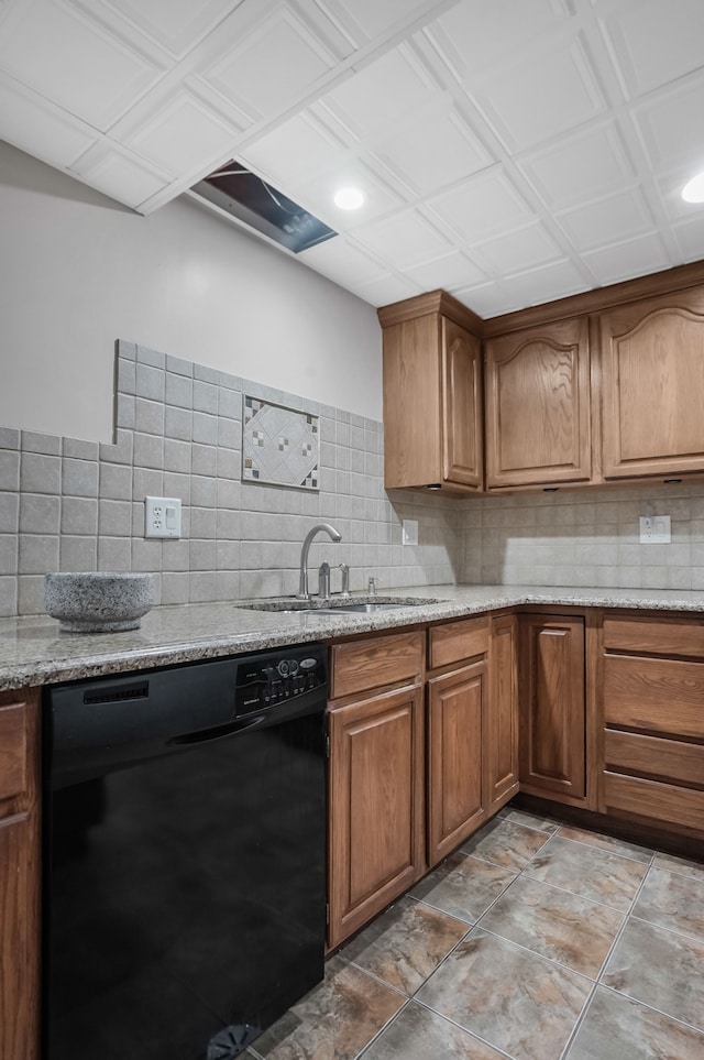 kitchen with tasteful backsplash, black dishwasher, sink, and light stone counters