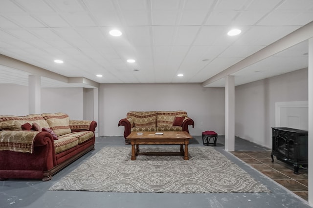 living room featuring a paneled ceiling, concrete floors, and a wood stove