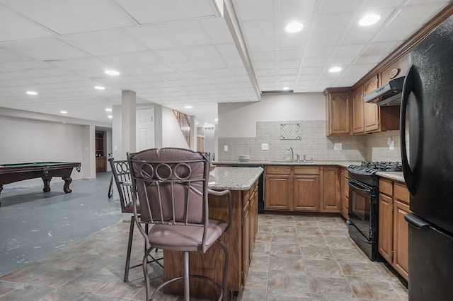 kitchen with tasteful backsplash, sink, a breakfast bar area, black appliances, and light stone countertops