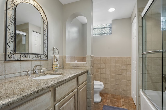 full bathroom with tile walls, tile patterned flooring, bath / shower combo with glass door, vanity, and toilet