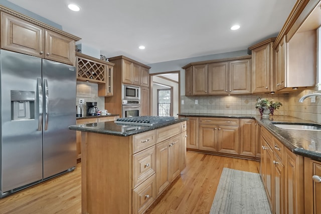 kitchen with dark stone counters, a sink, light wood-type flooring, stainless steel appliances, and a kitchen island