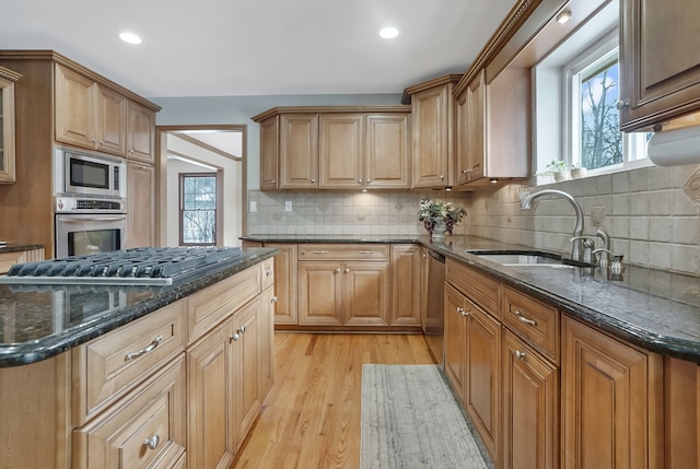 kitchen with appliances with stainless steel finishes, sink, dark stone countertops, backsplash, and light hardwood / wood-style flooring