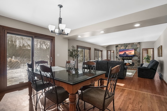 dining area featuring a stone fireplace, hardwood / wood-style floors, and an inviting chandelier