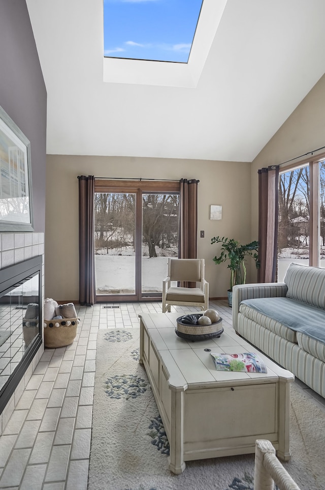 living room with a tiled fireplace and vaulted ceiling with skylight