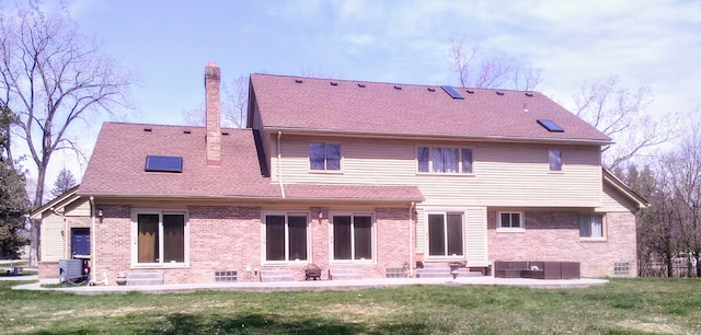 back of house featuring a chimney, brick siding, entry steps, and a yard