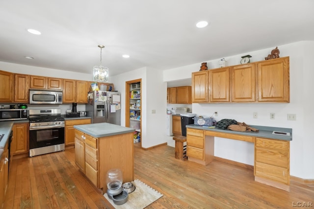 kitchen with washer / dryer, a center island, hanging light fixtures, appliances with stainless steel finishes, and hardwood / wood-style floors