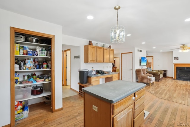 kitchen featuring a kitchen island, ceiling fan with notable chandelier, light wood-type flooring, and decorative light fixtures