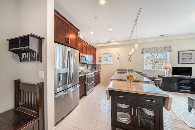 kitchen with appliances with stainless steel finishes, decorative light fixtures, rail lighting, an island with sink, and backsplash