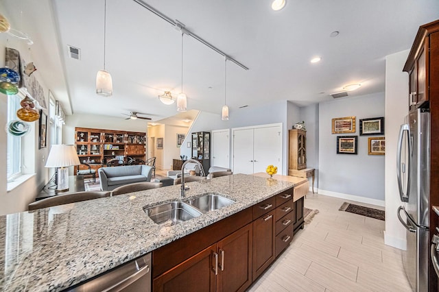 kitchen featuring stainless steel appliances, hanging light fixtures, sink, and light stone counters