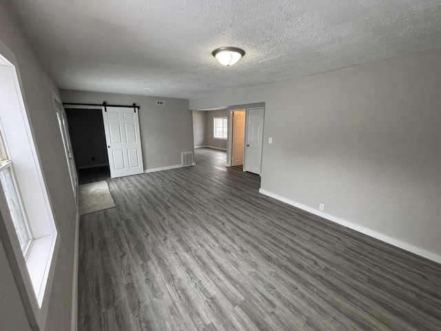 empty room with dark wood-type flooring, a barn door, and a textured ceiling