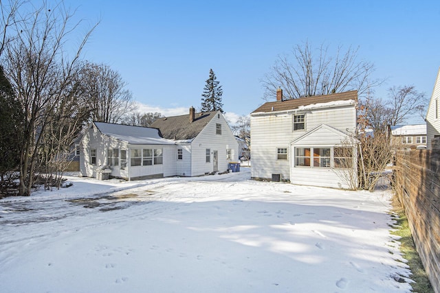 snow covered rear of property featuring a sunroom