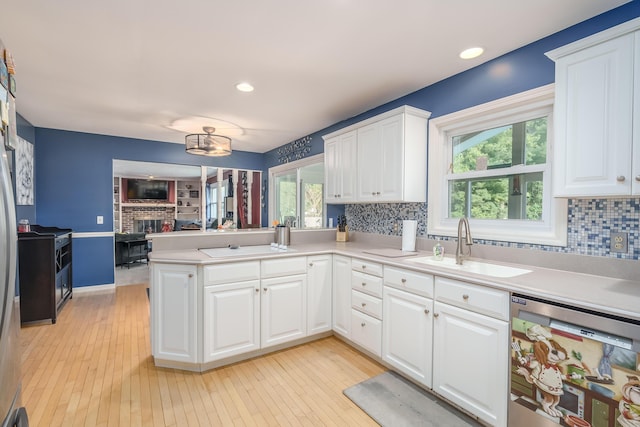 kitchen with dishwasher, sink, white cabinets, kitchen peninsula, and a brick fireplace