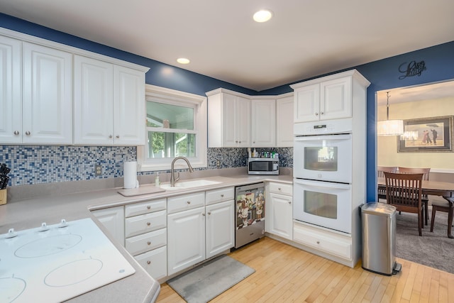 kitchen with tasteful backsplash, sink, white cabinets, stainless steel appliances, and light wood-type flooring