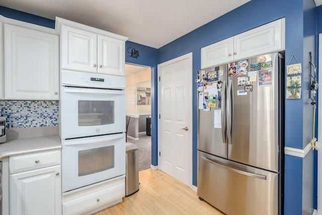 kitchen featuring white cabinetry, white double oven, backsplash, and stainless steel refrigerator