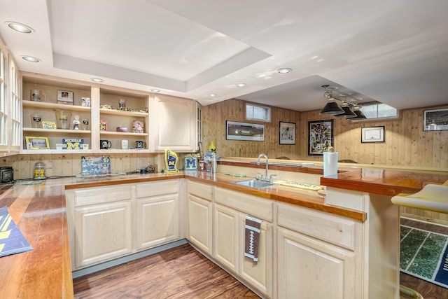 kitchen featuring wood walls, butcher block counters, sink, hardwood / wood-style flooring, and a raised ceiling