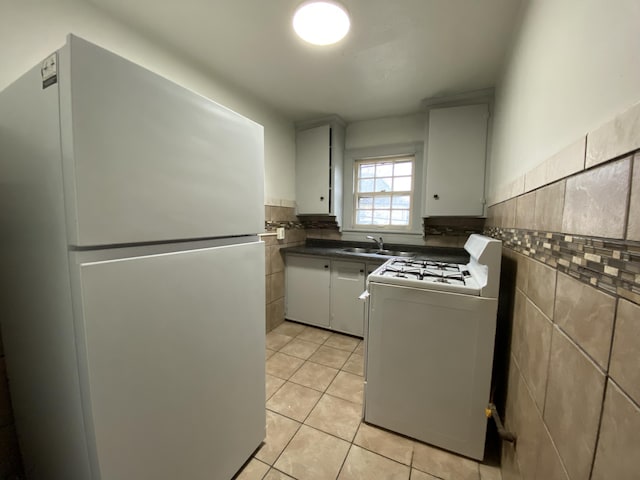 kitchen with light tile patterned flooring, sink, tile walls, white appliances, and white cabinets