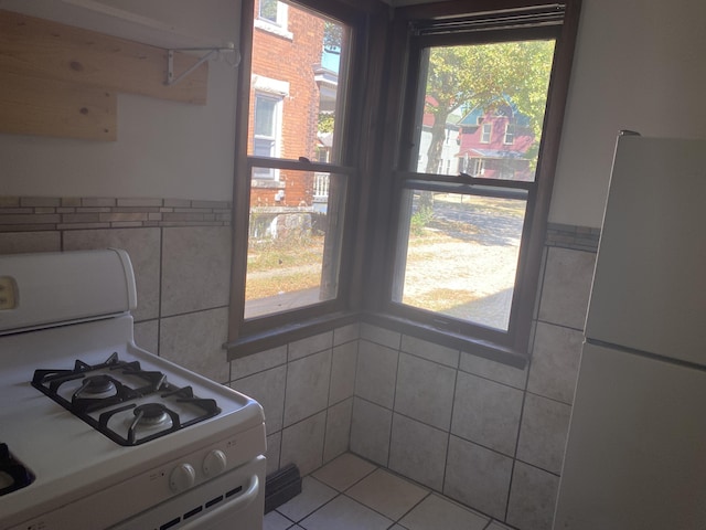 kitchen featuring white appliances, a healthy amount of sunlight, tile walls, and light tile patterned floors