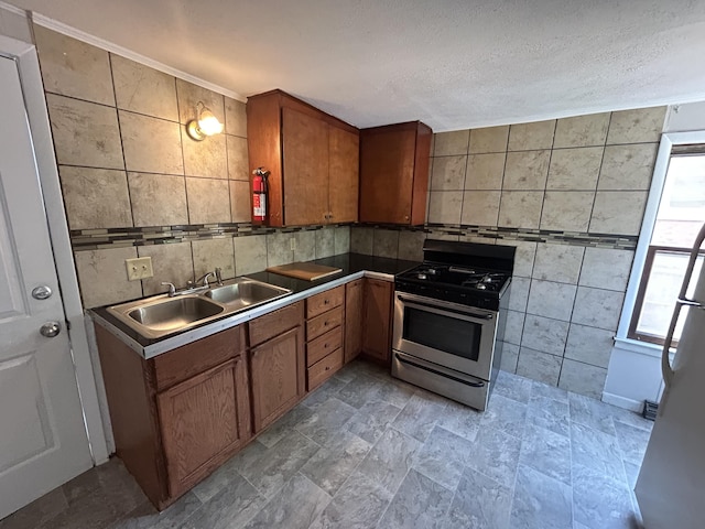 kitchen with stainless steel gas range oven, sink, tile walls, and a textured ceiling