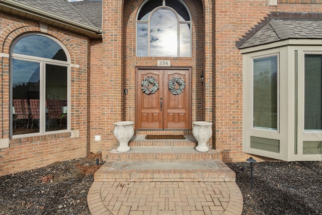 doorway to property with brick siding and a shingled roof