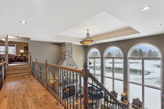 hallway with light wood finished floors, visible vents, a tray ceiling, an upstairs landing, and recessed lighting