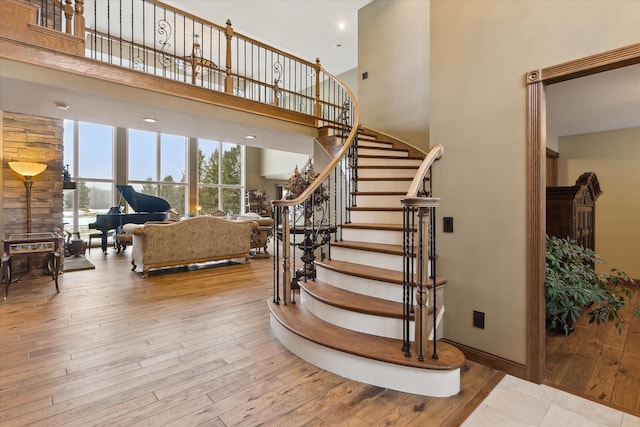 staircase with recessed lighting, wood finished floors, and a towering ceiling