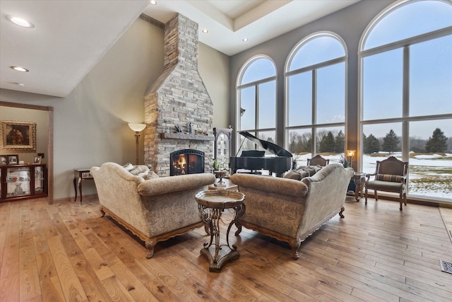 living room featuring light wood-style flooring, recessed lighting, a high ceiling, a stone fireplace, and baseboards