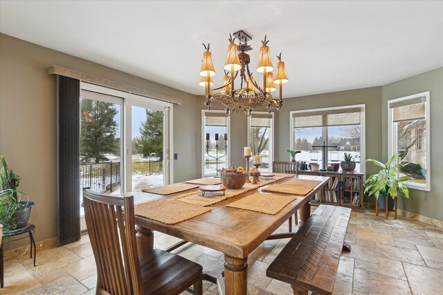 dining space featuring stone tile floors, a chandelier, and baseboards