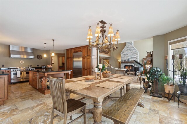 dining room with an inviting chandelier, a fireplace, and stone tile flooring