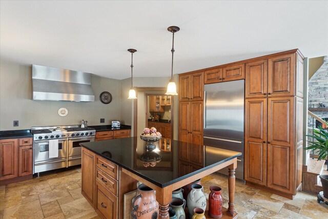 kitchen featuring dark countertops, high end appliances, wall chimney exhaust hood, and stone tile flooring