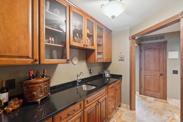 kitchen with a sink, stone finish flooring, brown cabinets, and glass insert cabinets