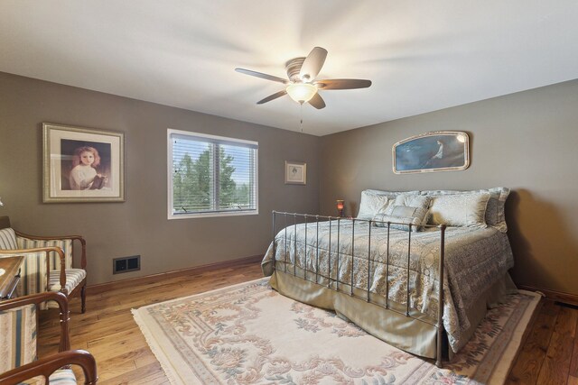 bedroom featuring baseboards, wood-type flooring, visible vents, and a ceiling fan