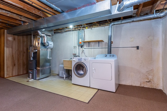 laundry area with wooden walls, electric panel, heating unit, washer and dryer, and light carpet