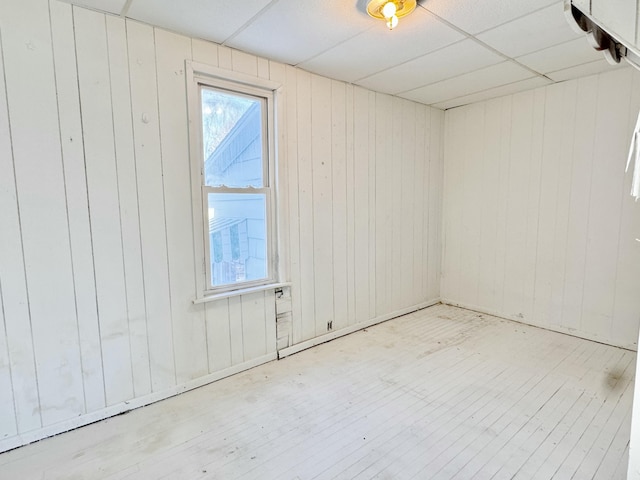 spare room with a paneled ceiling, wooden walls, light hardwood / wood-style flooring, and a wealth of natural light