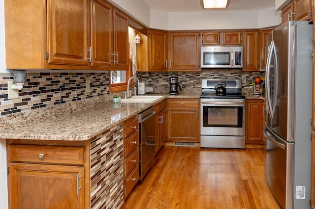 kitchen with sink, appliances with stainless steel finishes, tasteful backsplash, light stone countertops, and light hardwood / wood-style floors