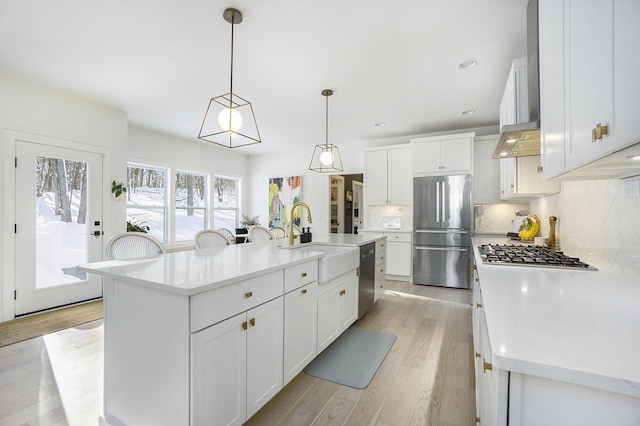 kitchen featuring decorative light fixtures, an island with sink, white cabinetry, sink, and stainless steel appliances