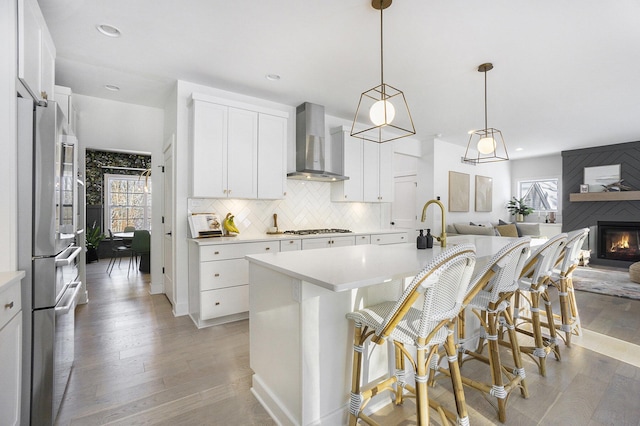 kitchen featuring wall chimney exhaust hood, a breakfast bar area, white cabinetry, hanging light fixtures, and a kitchen island with sink